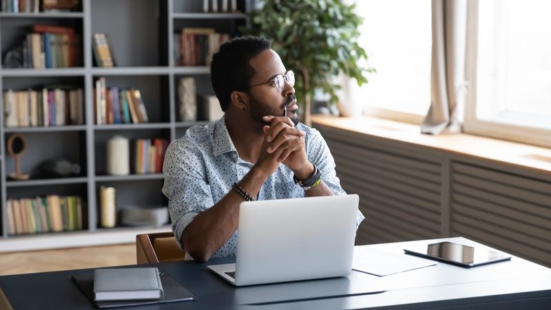 How to Get Accredited to Work in Canada african american man thinking in front of laptop | work in Canada