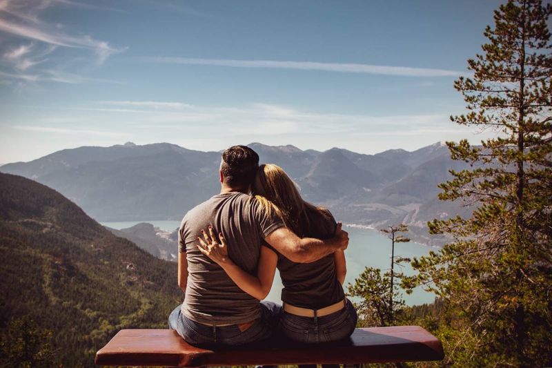 man and woman in love sitting on bench looking at landscape
