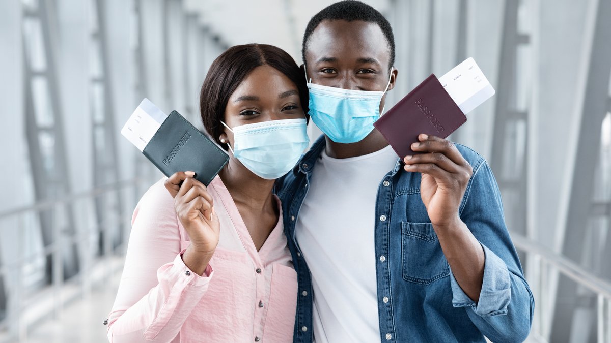 Black couple in protective medical masks posing with passports and tickets at airport