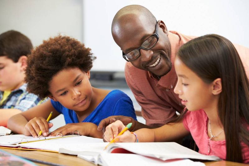 Immigrate to Canada as a Teacher smiling male teacher helping students at desks in classroom | move to Canada