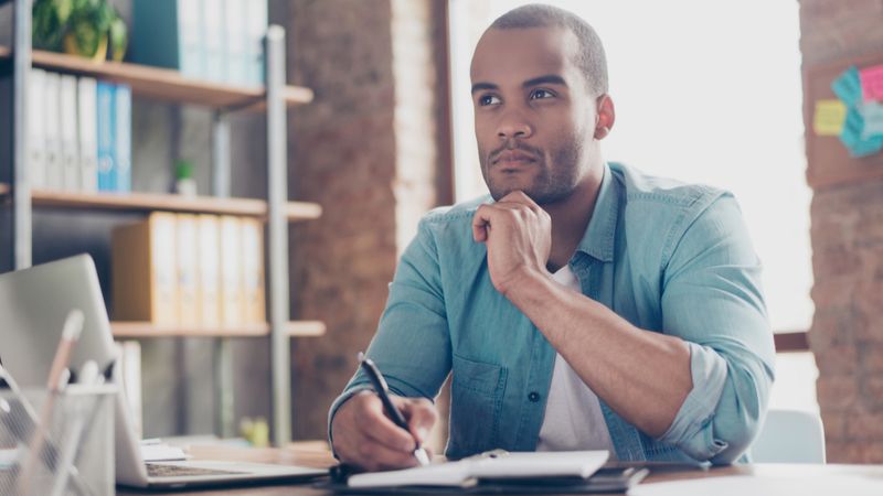 unsure man writing in journal  and working on laptop | Express Entry profile